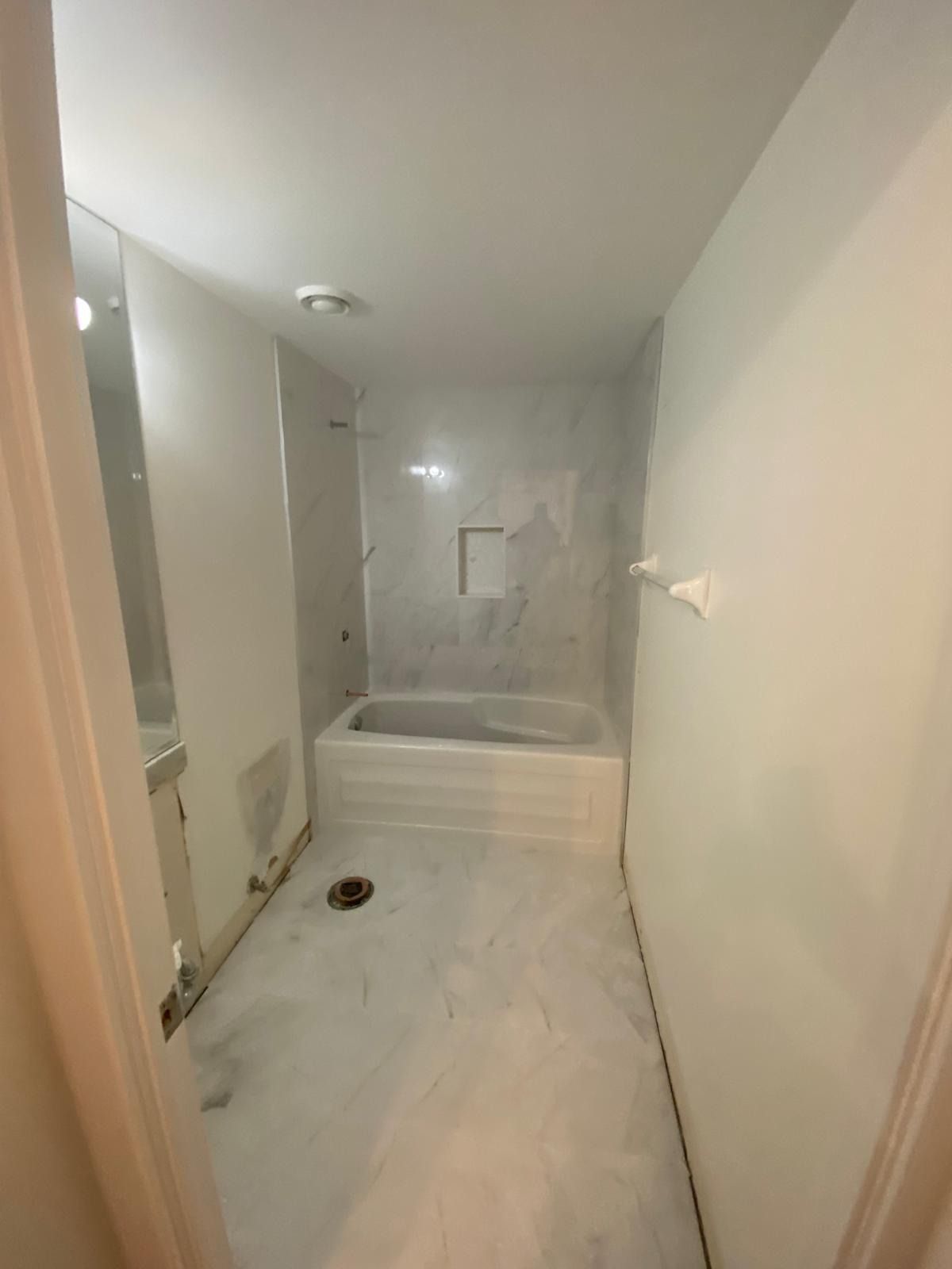 Basement bathroom with marble-look floor tile and a tiled tub surround