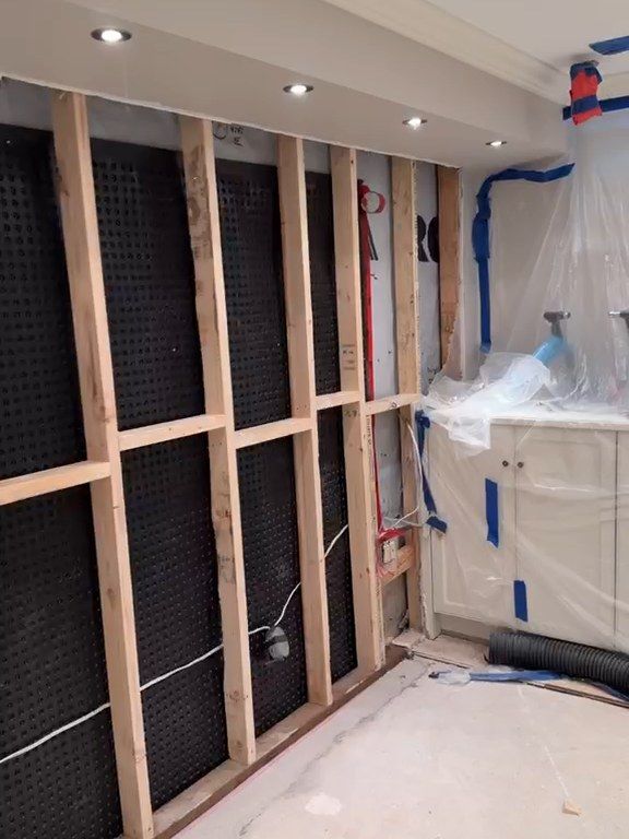 Basement wall framed in new wood studs over a black dimpled membrane, under a finished ceiling with pot lights