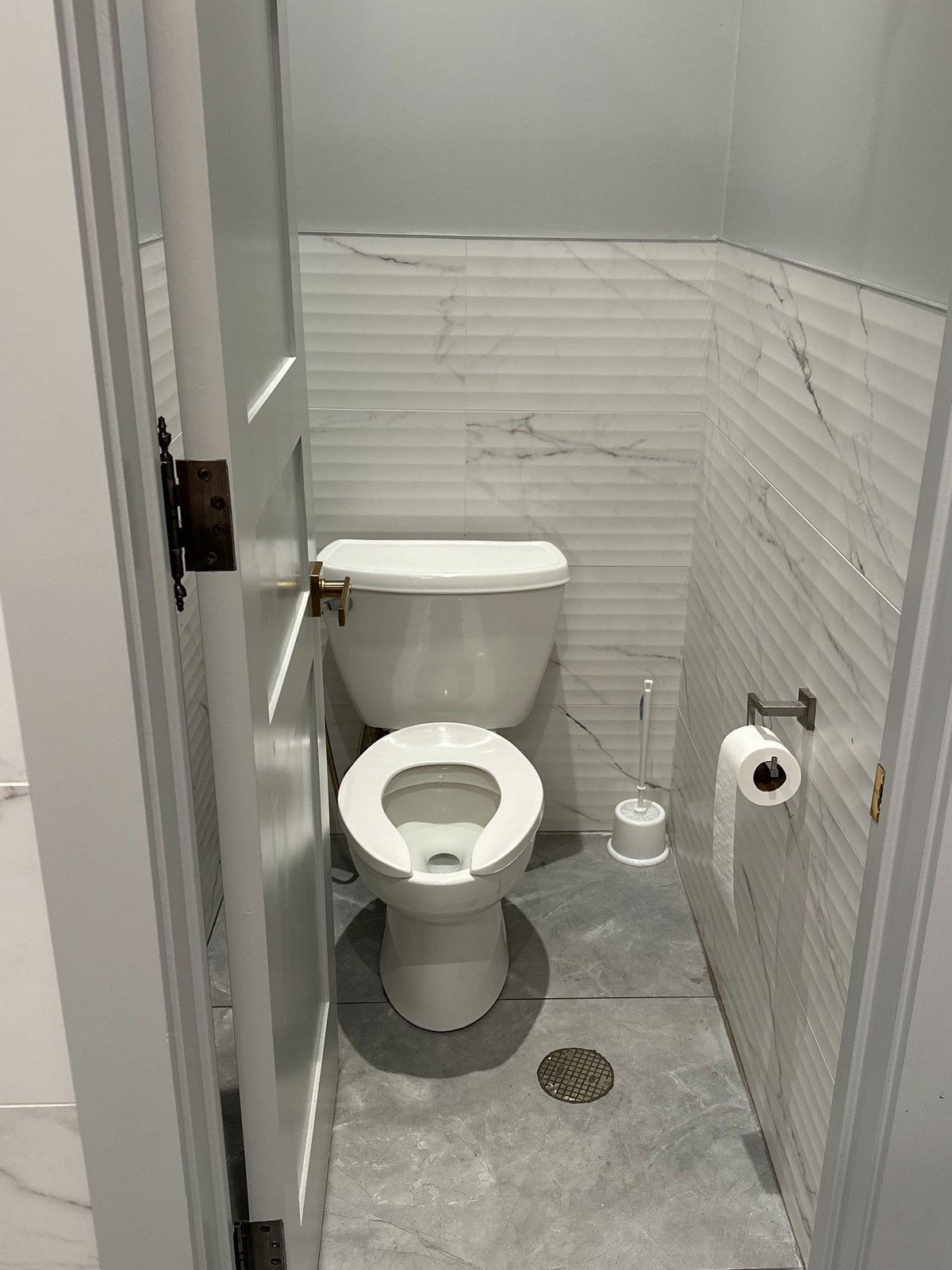A separate toilet room with ribbed white marble-look wall tile, pale grey paint above it and a grey tile floor with a drain
