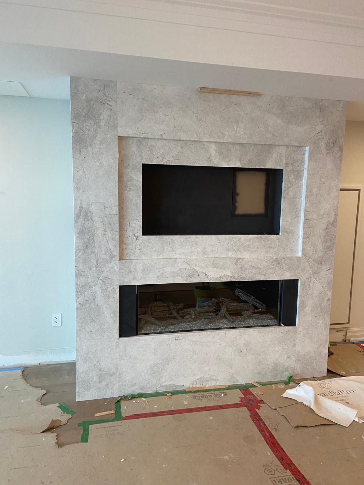 Fireplace wall clad in grey-veined porcelain slabs with a TV niche above a linear fireplace
