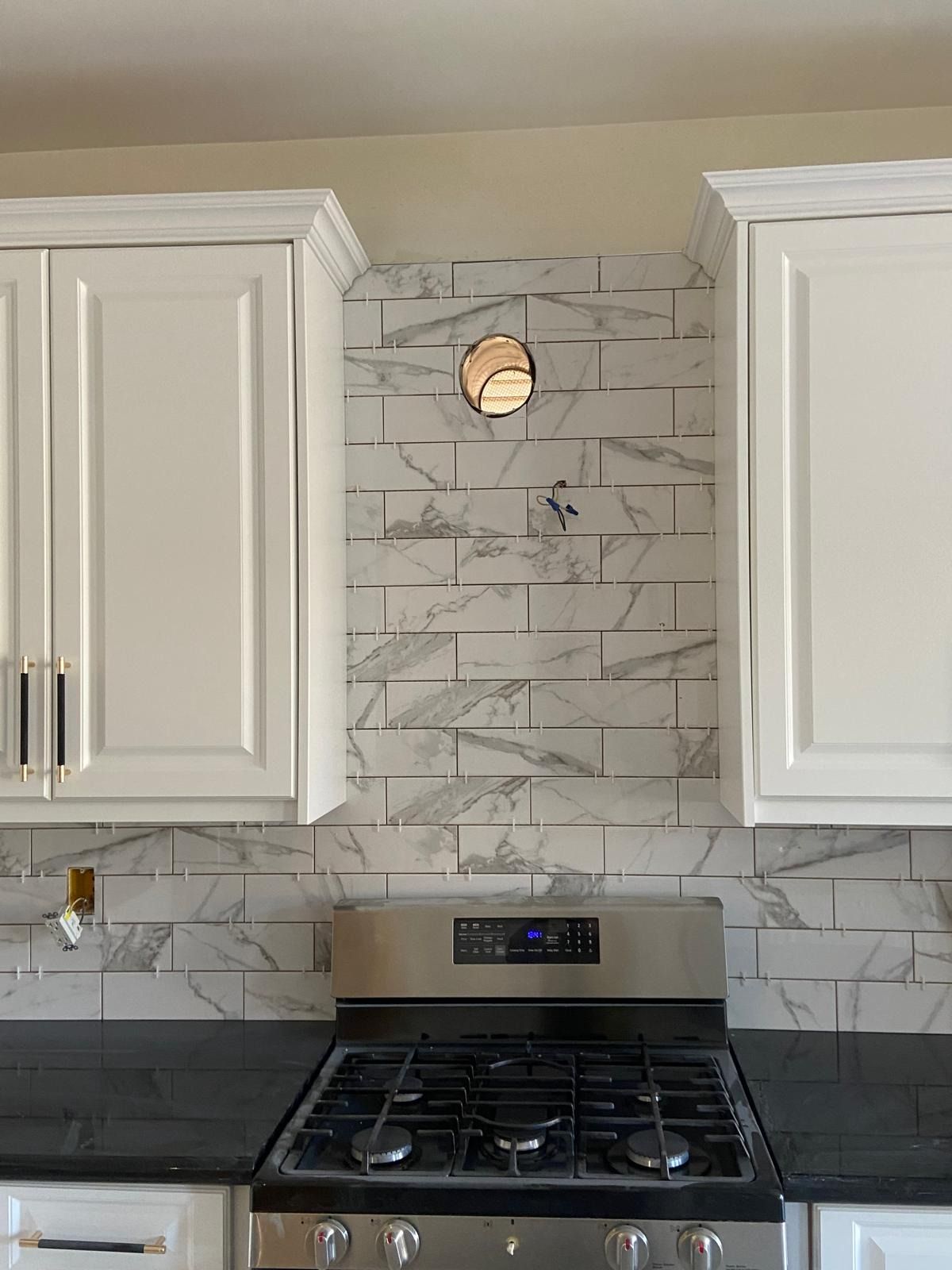 Marble-look subway tile backsplash between white cabinets, run up to the top of the cabinets