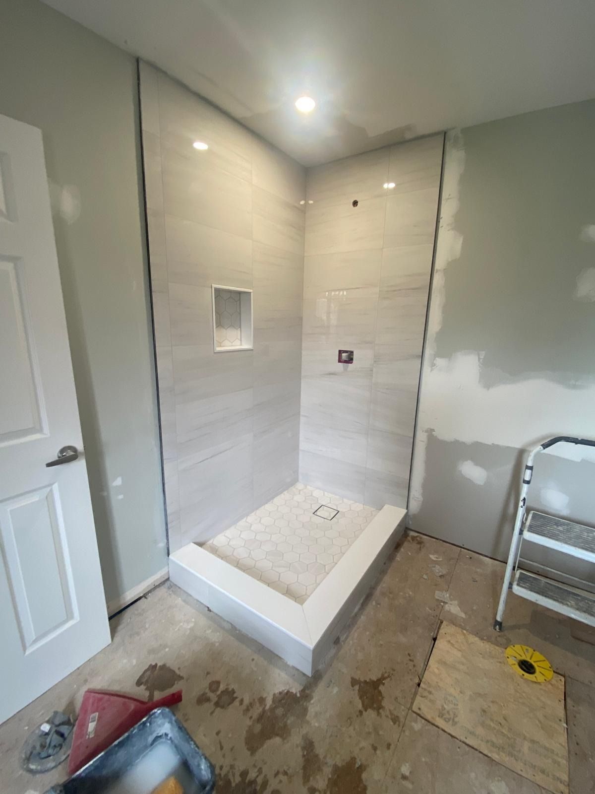 Corner shower in grey plank-pattern tile with a white hex mosaic floor
