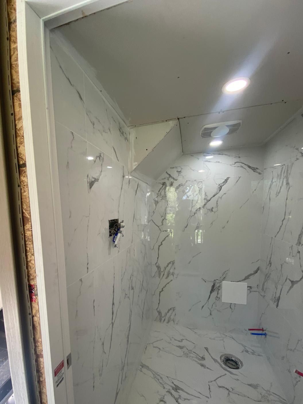 Shower lined floor to ceiling in white marble-look porcelain with grey veining